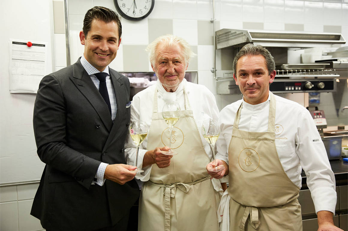 two chefs and a man in a suit holding glasses of champagne smiling at the camera