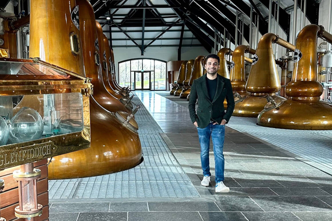 A man standing in a whiskey factory wearing jeand and a grey jacket