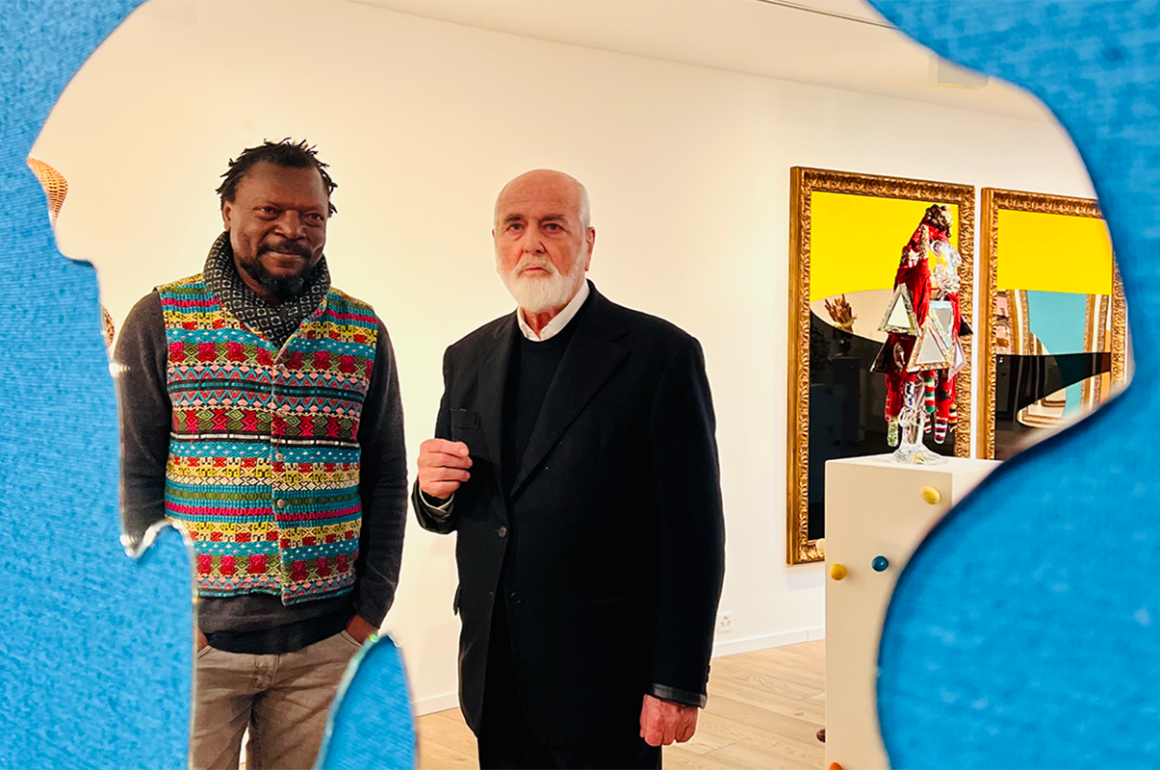 Two artists who are men standing in front of a mirror with a blue background