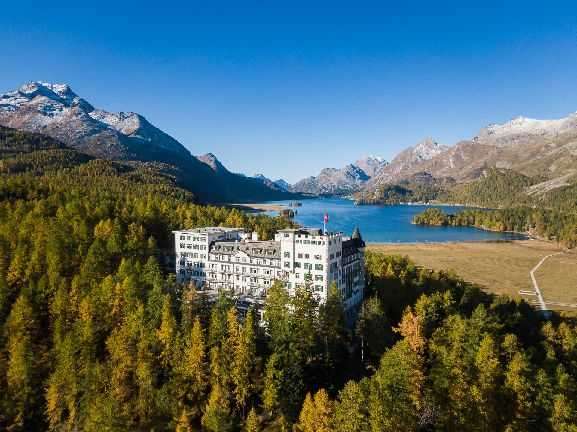 white building in the middle of a forest with lake behind